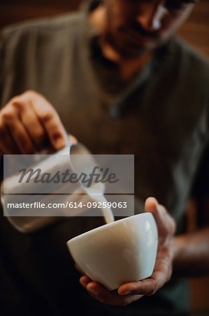 Barista pouring milk into coffee cup in cafe, cropped shallow focus