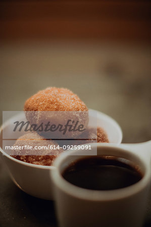 Cup of black coffee and bowl of doughnuts on cafe table, close up shallow focus