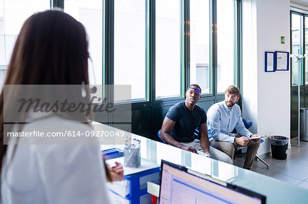 Nurse speaking with patients completing forms at hospital reception