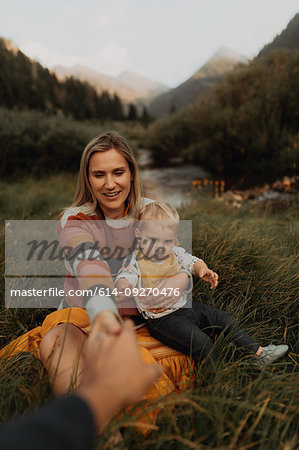 Mid adult couple sitting with toddler daughter holding hands by rural river, Mineral King, California, USA