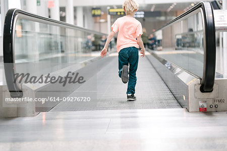 Boy running on moving walkway in airport, full length rear view