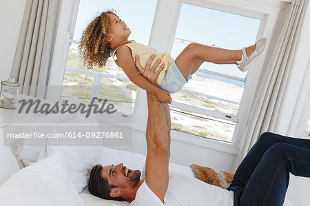 Father lifting daughter in mid air on bed in beach house