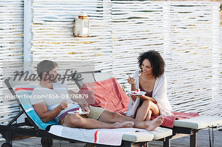 Couple talking and enjoying raspberry cake on deckchairs