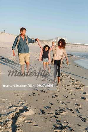 Couple swinging daughter in mid air on sandy beach