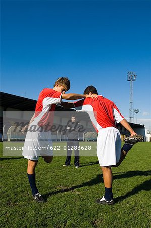 Two boys stretching as the coach looks on