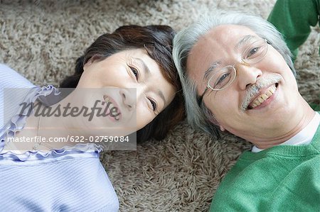 Senior couple lying head to head on carpet