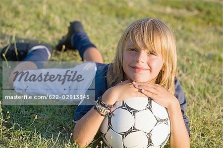 Boy smiling and lying on grass with soccer ball