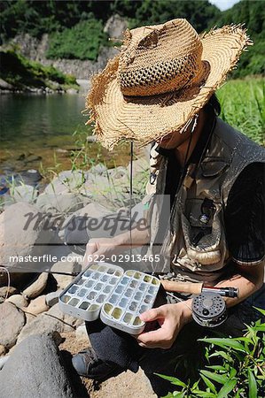 Man with straw hat sitting on stone and holding fly box