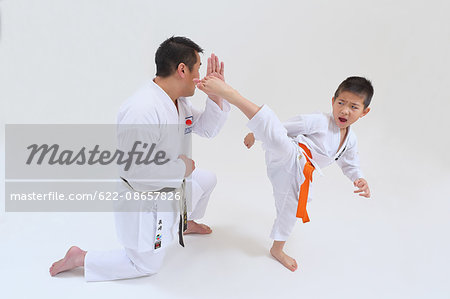 Japanese kid in karate uniform training with teacher on white background