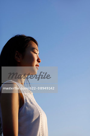 Young Japanese woman in a white dress at a cliff over the sea at sunrise, Chiba, Japan