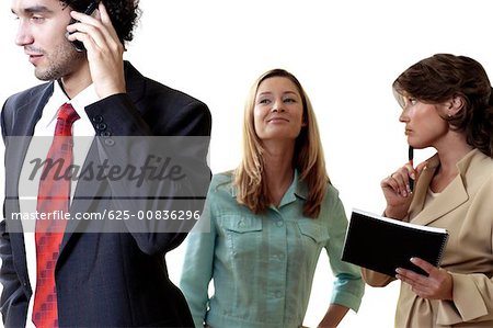 Businessman talking on a mobile phone with his two secretaries standing behind him