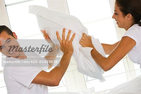 Side profile of a young couple having a pillow fight