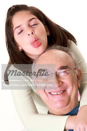 Close-up of a granddaughter sticking out her tongue and hugging her grandfather