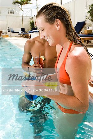 Side profile of a young woman and a young man holding glasses in a swimming pool