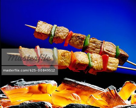 Close-up of meat on a skewer cooking above coal