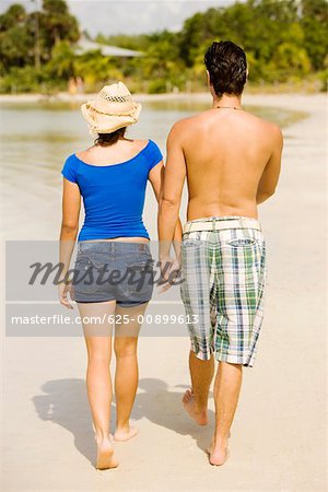 Rear view of a young man and a teenage girl walking on the beach