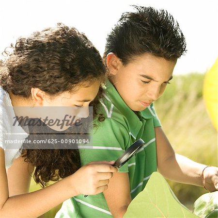 Close-up of a boy and a girl looking through a magnifying glass
