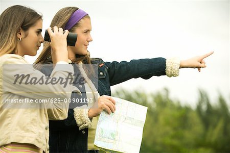 Teenage girl pointing forward with a girl looking through a pair of binoculars
