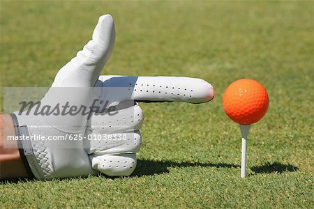 Close-up of a person's hand pointing at a golf ball on a golf tee