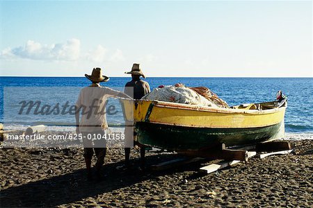 Rear view of two men near a boat on a beach on the island of Martinique, Caribbean