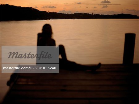 Silhouette of a young woman sitting on pier