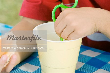 Mid section view of a child holding a burger and drinking with a straw