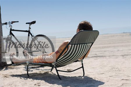 Rear view of a man reclining on a lounge chair on the beach