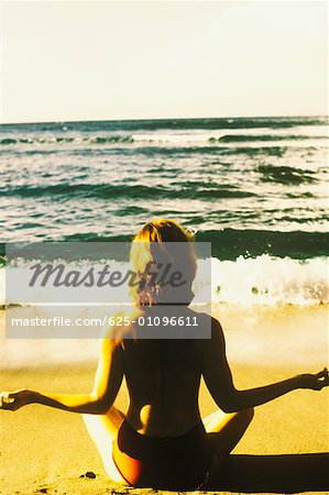 Rear view of a woman sitting in the lotus position on the beach, Caribbean