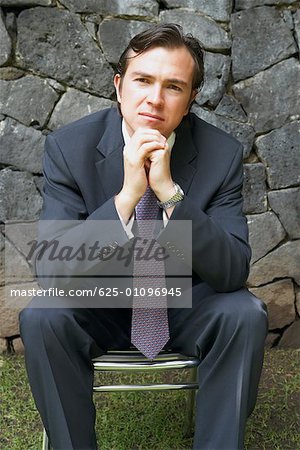 Close-up of a businessman sitting on a chair in front of a stone wall