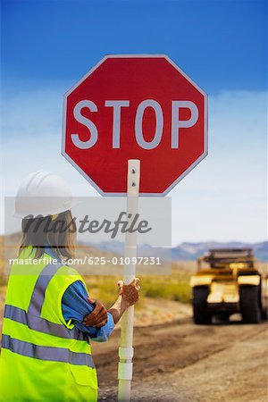 Rear view of a man holding a stop sign on a dirt road