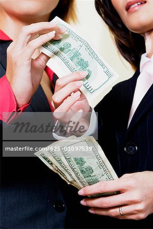 Mid section view of a businesswoman giving one hundred dollar bill to another businesswoman