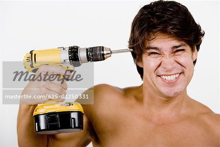 Portrait of a mid adult man holding a drill machine against his head