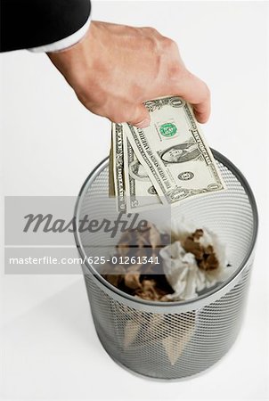 Close-up of a businessman's throwing paper currency in a wastepaper basket