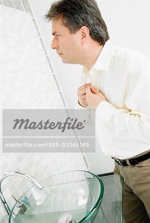 Side profile of a mature man buttoning his shirt in the bathroom