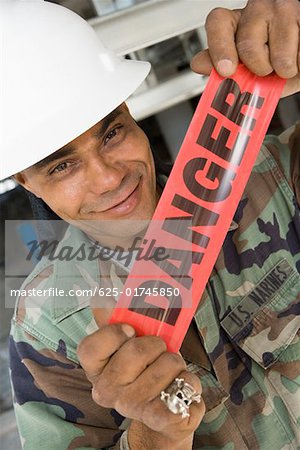 Portrait of a male construction worker holding a cordon tape and smirking