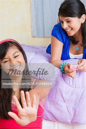 Teenage girl looking at polished nails and a young woman lying on the bed behind her