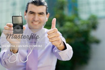 Portrait of a businessman showing an MP3 player and making a thumbs up sign