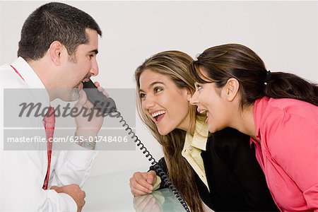 Side profile of a businessman talking on the telephone with two businesswomen looking at him and smiling