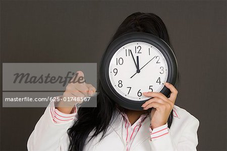 Close-up of a businesswoman holding a clock in front of her face and pointing