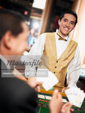 Rear view of a mature man holding playing cards with a casino worker standing in front of him