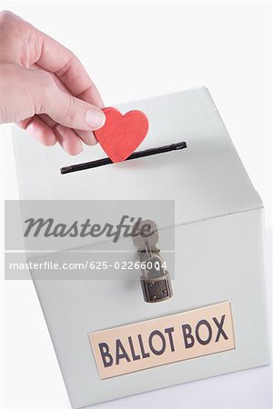 Close-up of a person's hand inserting a heart shaped vote into a ballot box