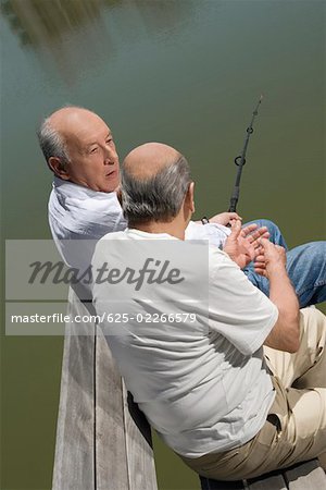 High angle view of two senior men sitting on a bench at a lakeside and fishing