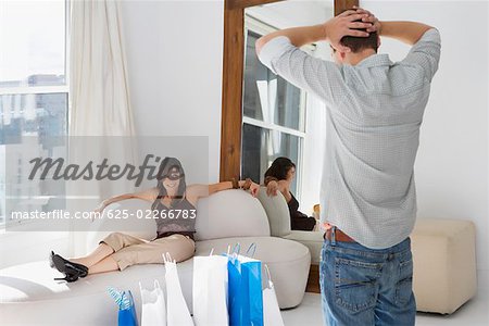 Young woman reclining on a couch with a young man standing with his hands behind his head