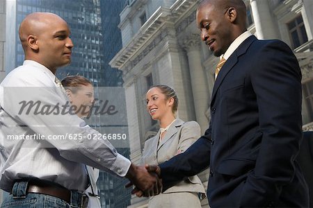 Side profile of two businessmen shaking hands with two businesswomen smiling