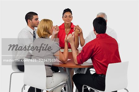 Three businessmen and two businesswomen praying with holding their hands in a meeting