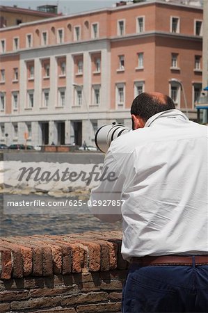Rear view of a man with a hand-held telescope, Via Partenope, Bay of Naples, Naples, Naples Province, Campania, Italy