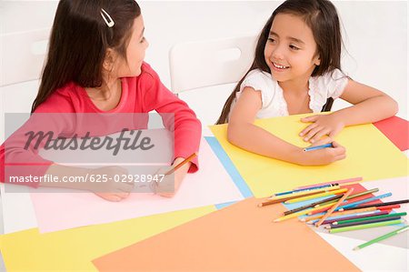 High angle view of two schoolgirls drawing together in a classroom