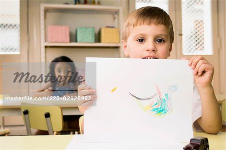 Portrait of a boy showing a drawing with a girl drawing in the background