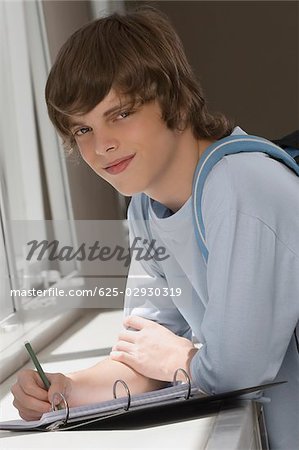 Portrait of a teenage boy writing on spiral notebook and smiling