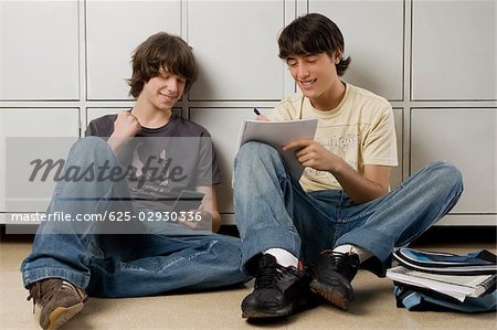 Young man sitting with a teenage boy and writing on a notebook